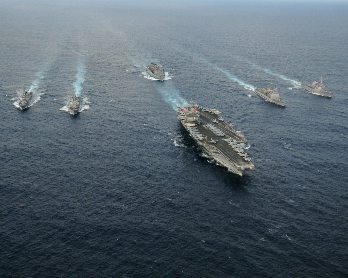 A U.S. Navy carrier strike group underway, an aircraft carrier flanked by escort ships.